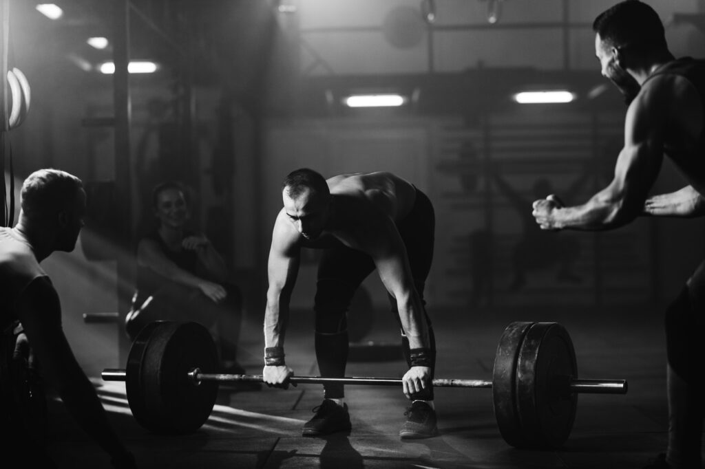 Muscular build man exercising deadlift on weight training with support of his friends.